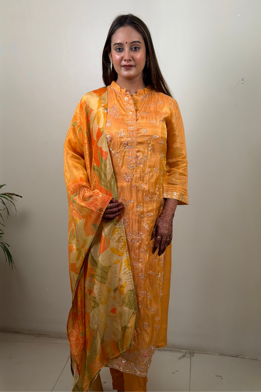 Woman wearing an orange traditional outfit with a floral pattern against a plain background