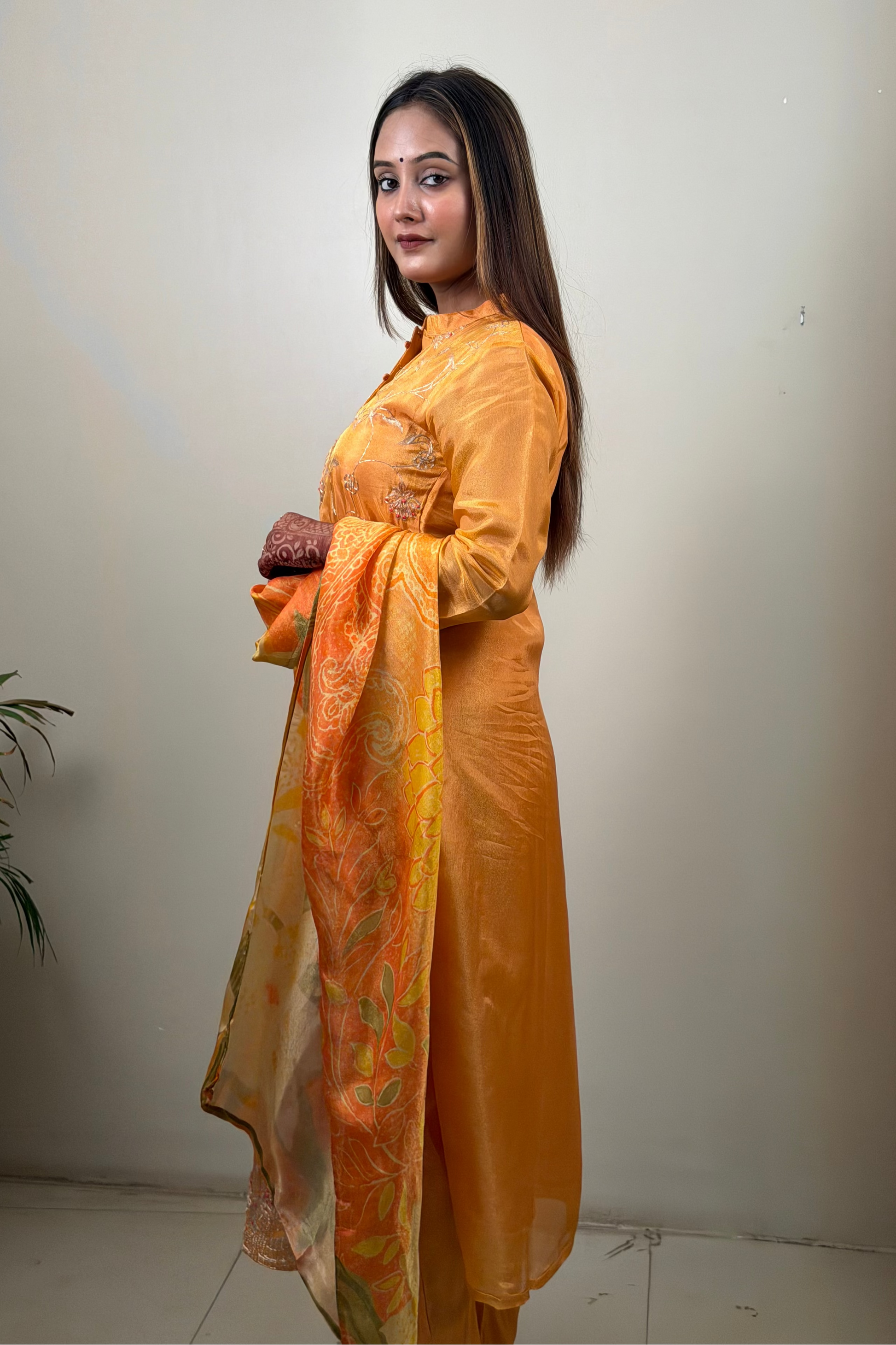 Woman in a yellow traditional outfit with a matching dupatta against a plain background