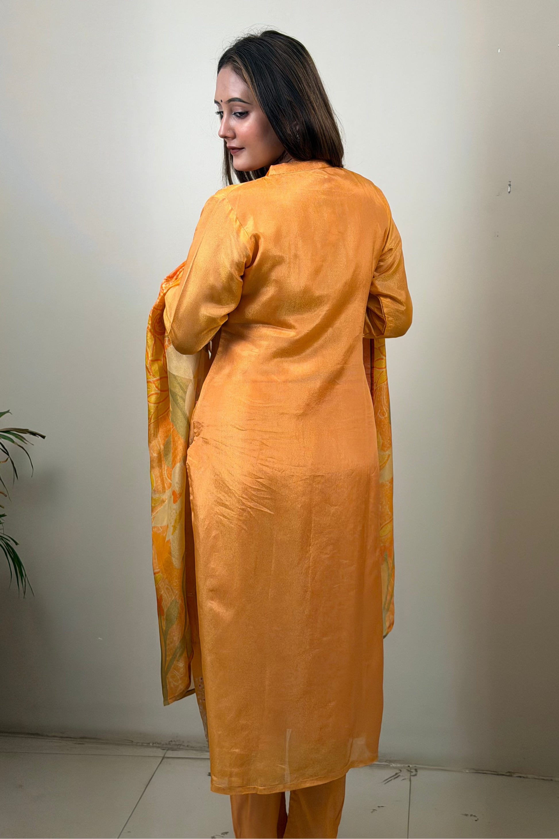 Woman wearing an orange kurta with a matching dupatta against a plain white wall.