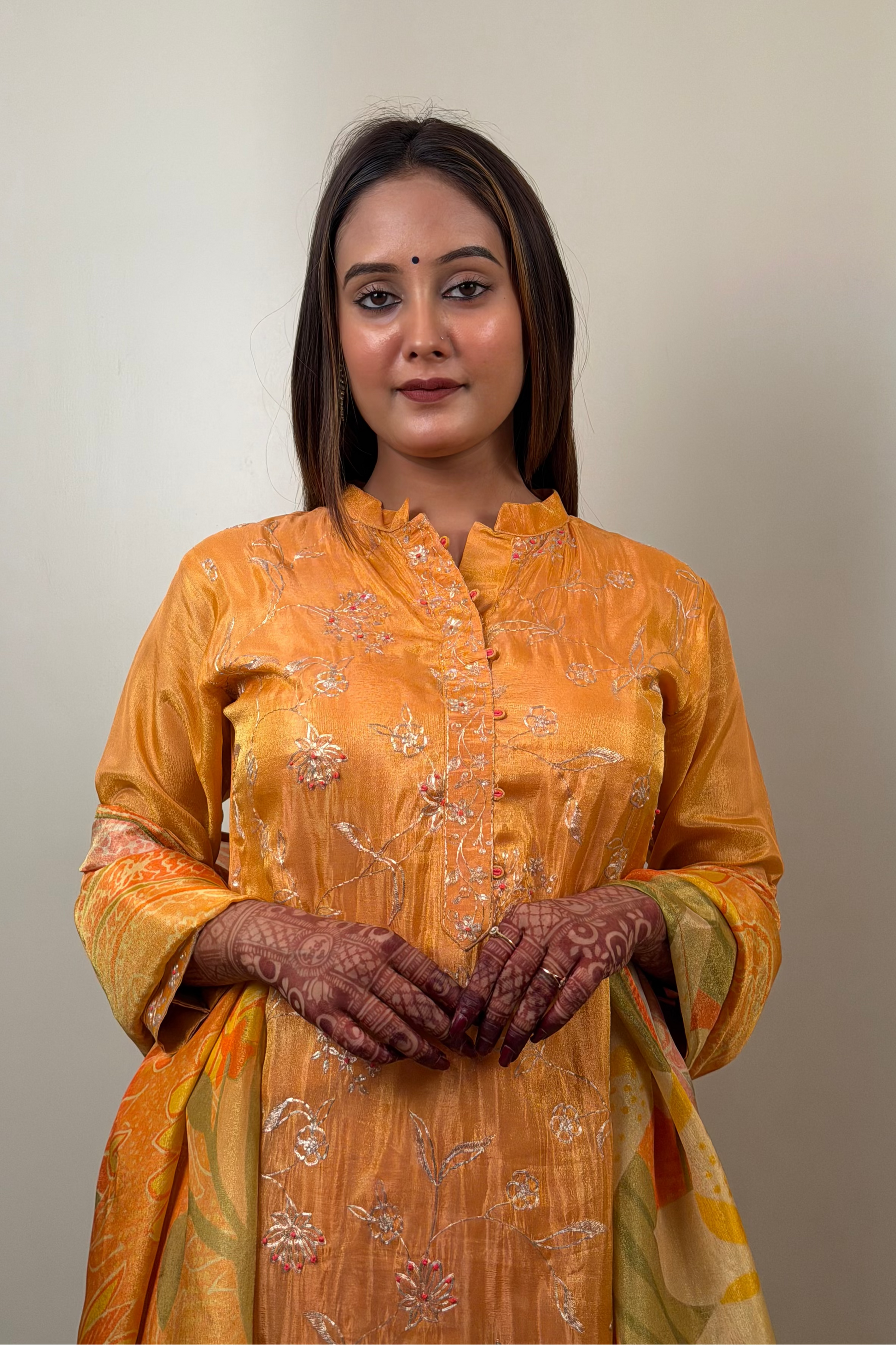 Woman wearing an orange traditional outfit with floral patterns against a plain background