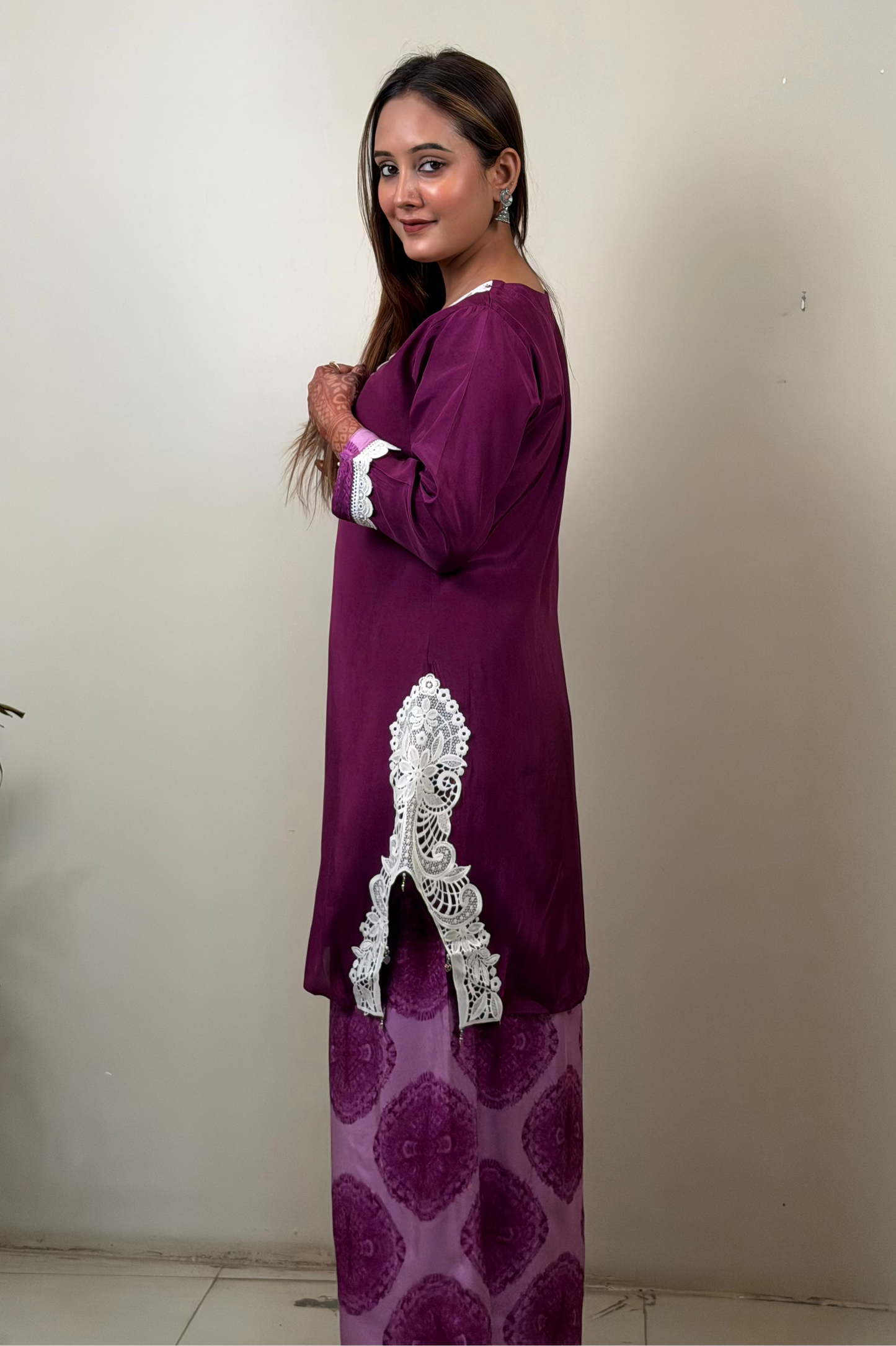 Woman wearing a purple traditional outfit with white embroidery against a plain background