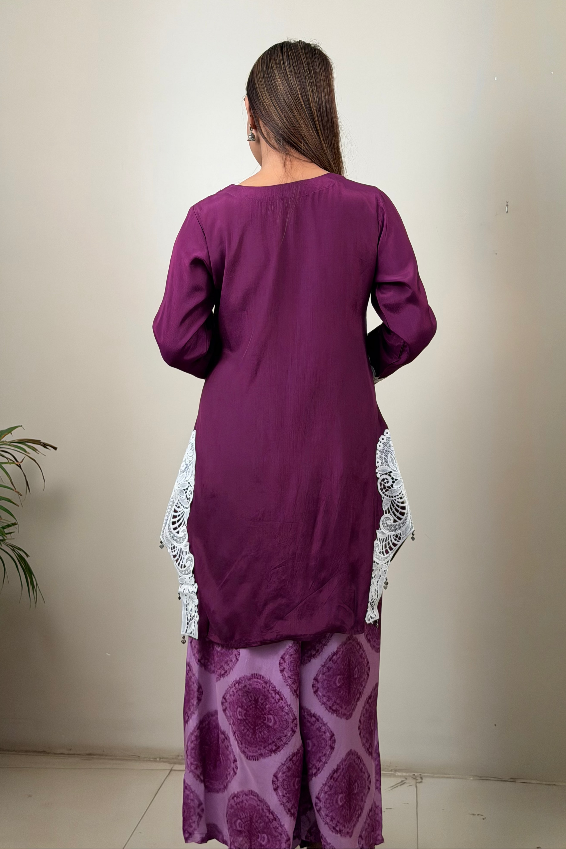 Woman wearing a purple outfit with white lace details against a plain background