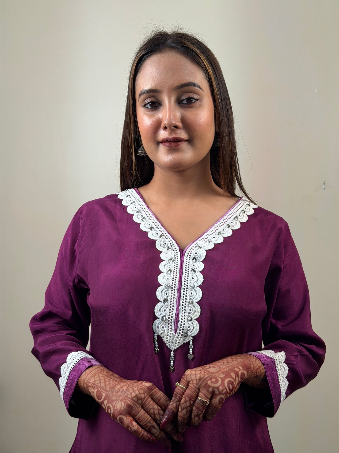 Woman wearing a purple traditional outfit with white lace details on a plain background