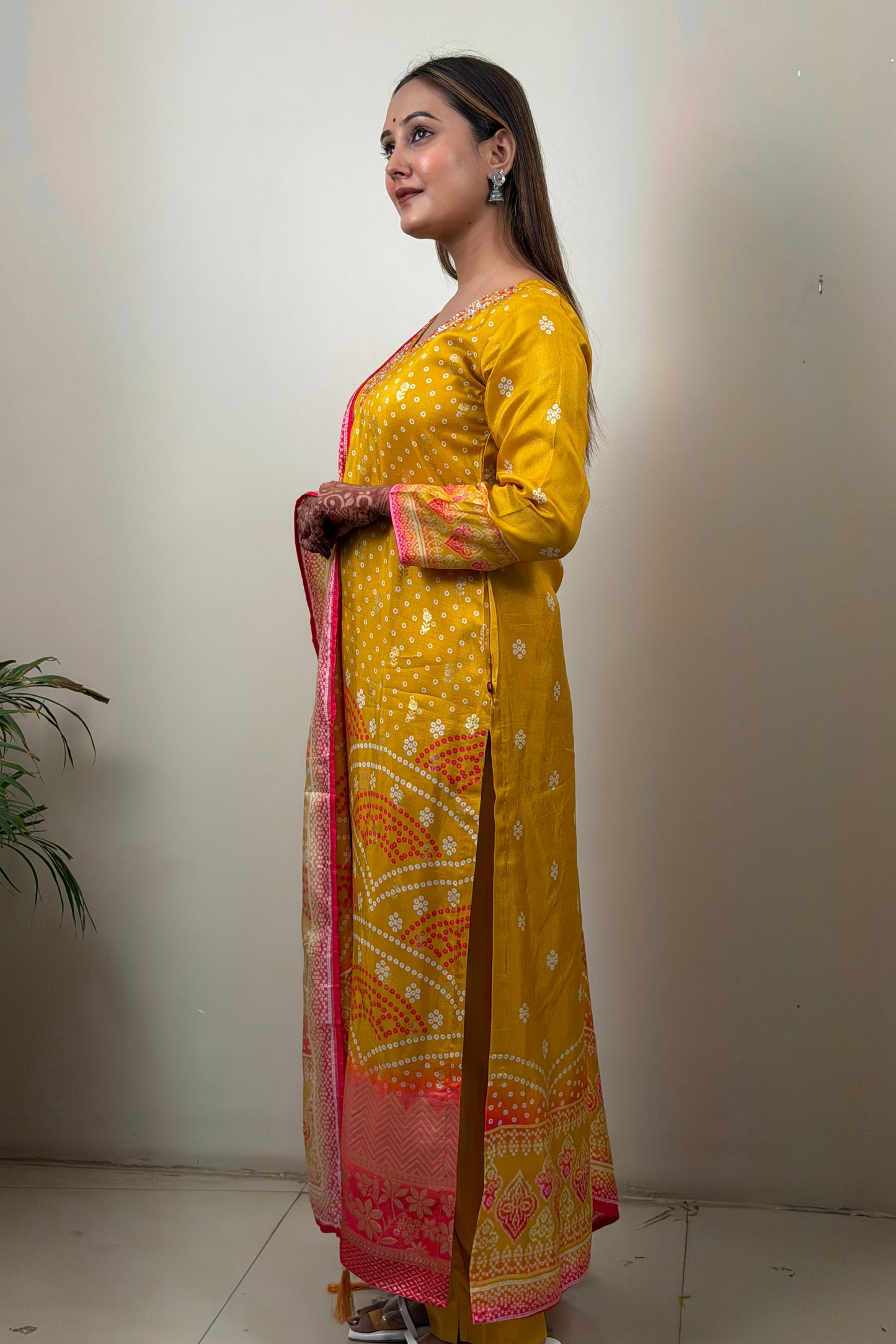 Woman in a yellow traditional outfit with a pink and white dupatta against a plain background