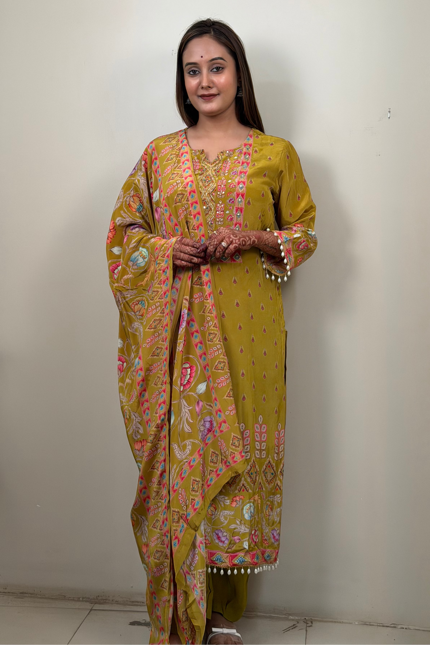 Woman wearing a yellow patterned saree standing against a plain wall.