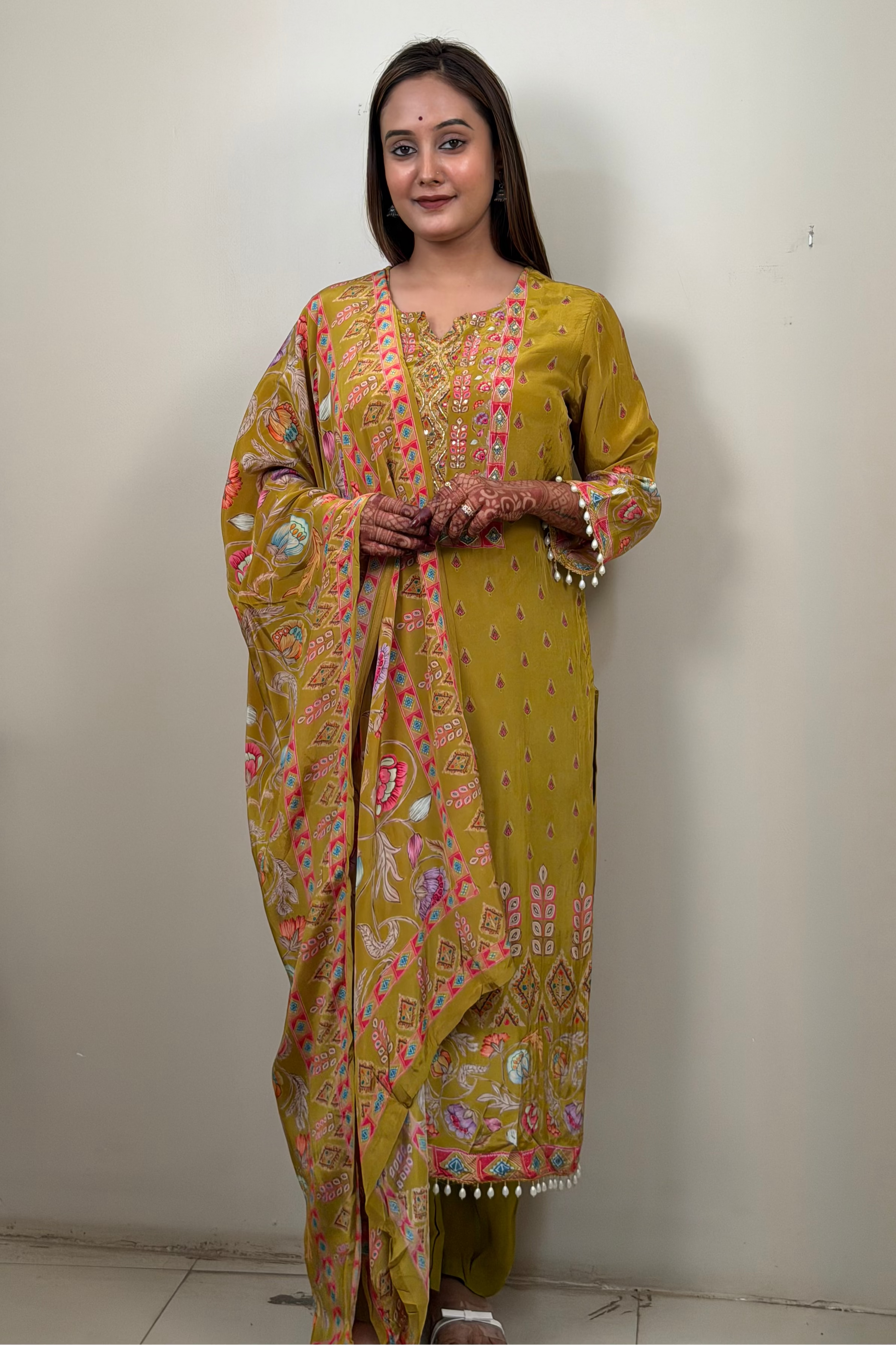 Woman wearing a yellow patterned saree standing against a plain wall.