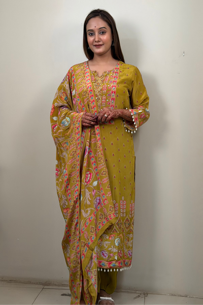 Woman wearing a yellow patterned saree standing against a plain wall.