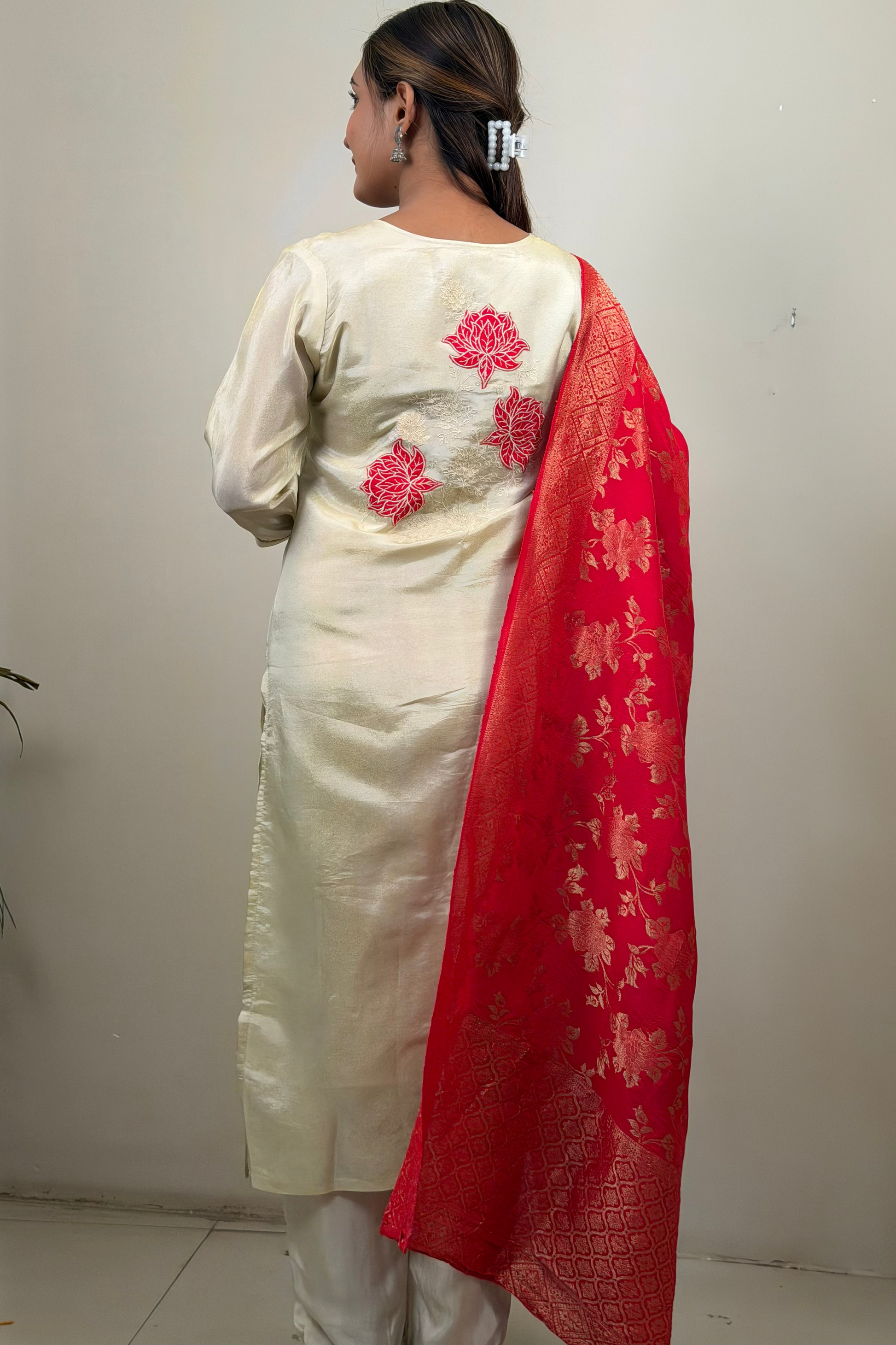 Woman wearing a cream kurta with red floral patterns and a red dupatta against a white wall.