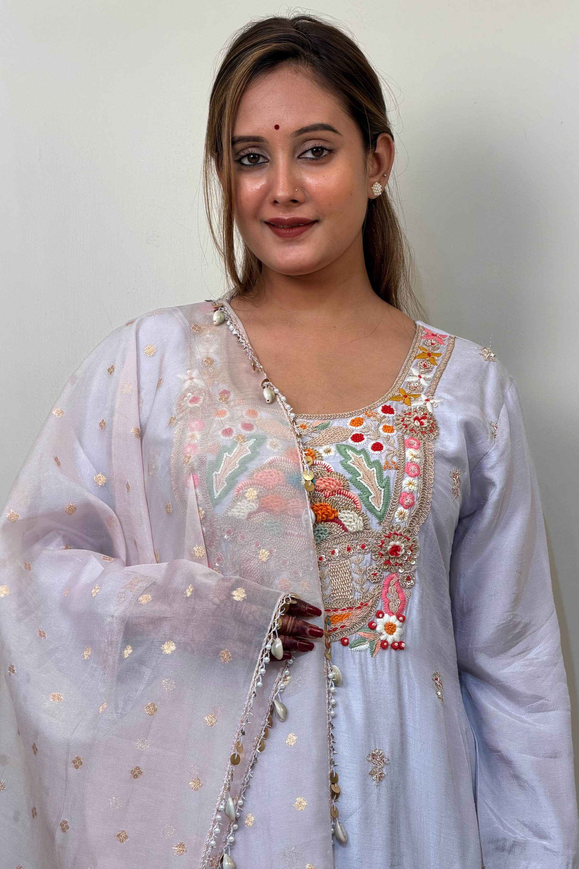 Woman wearing a traditional embroidered outfit with a sheer dupatta against a plain background