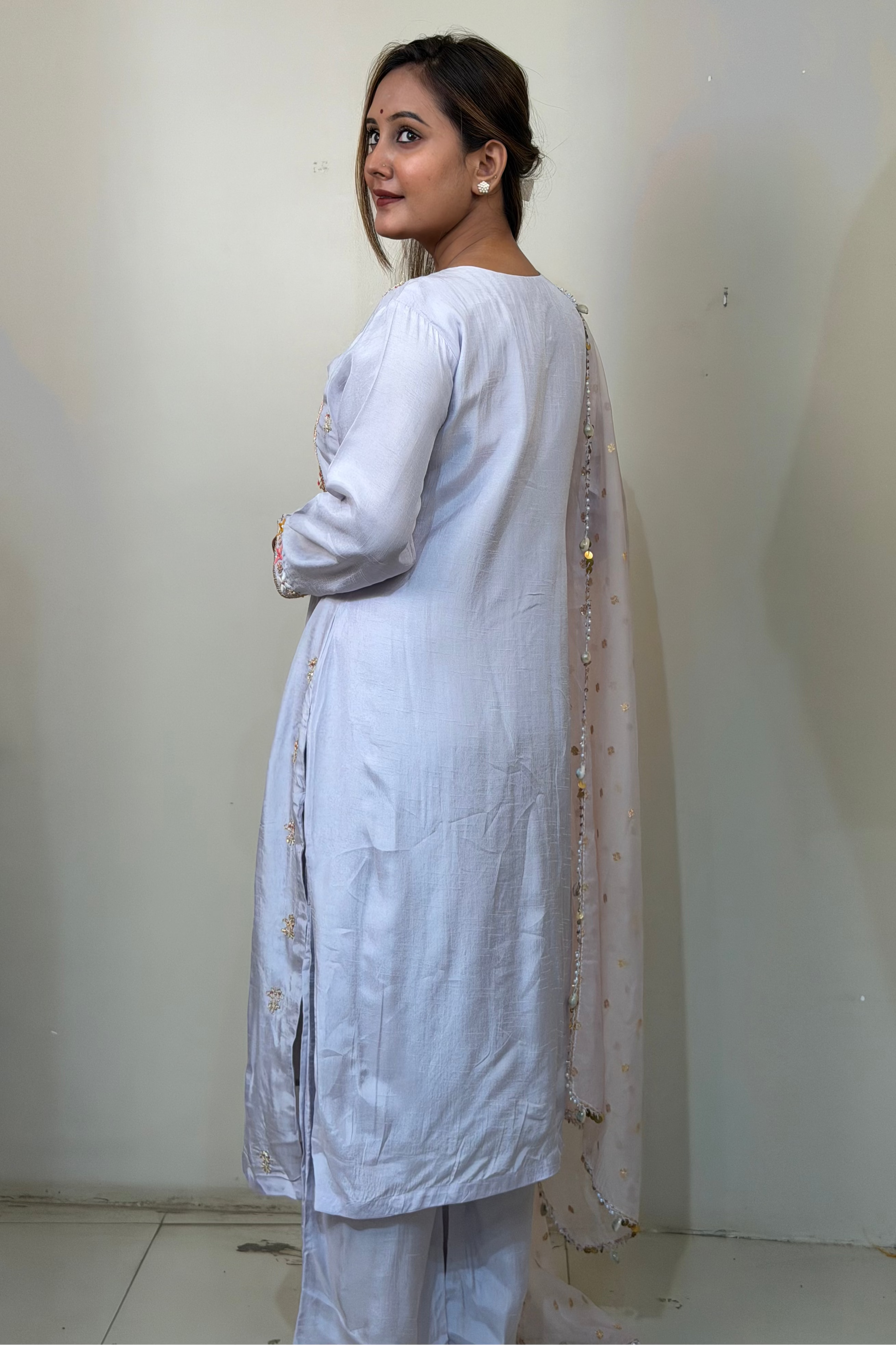 Woman wearing a light blue kurta with a matching dupatta against a white wall.
