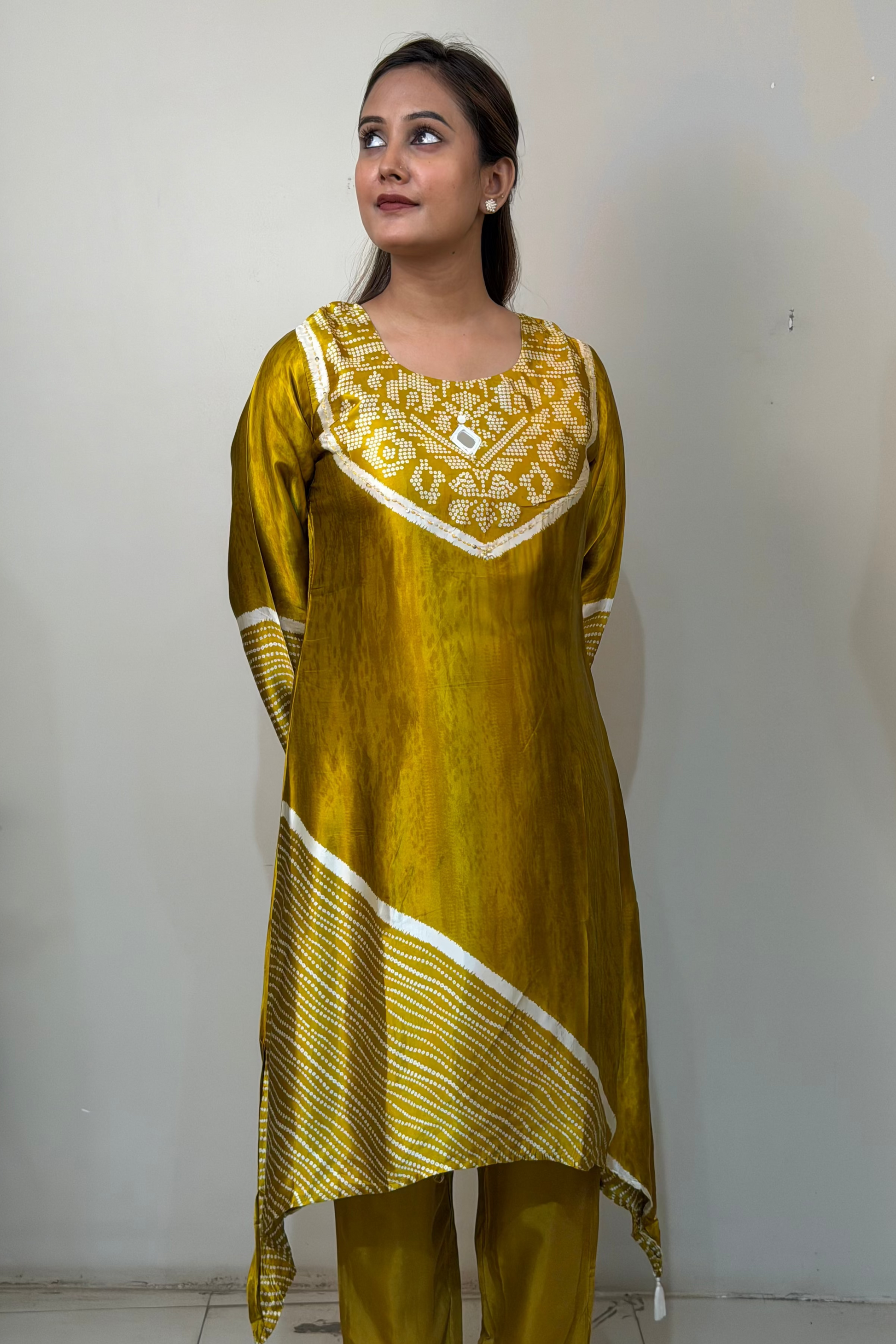 Woman wearing a yellow traditional outfit with white patterns against a plain wall.