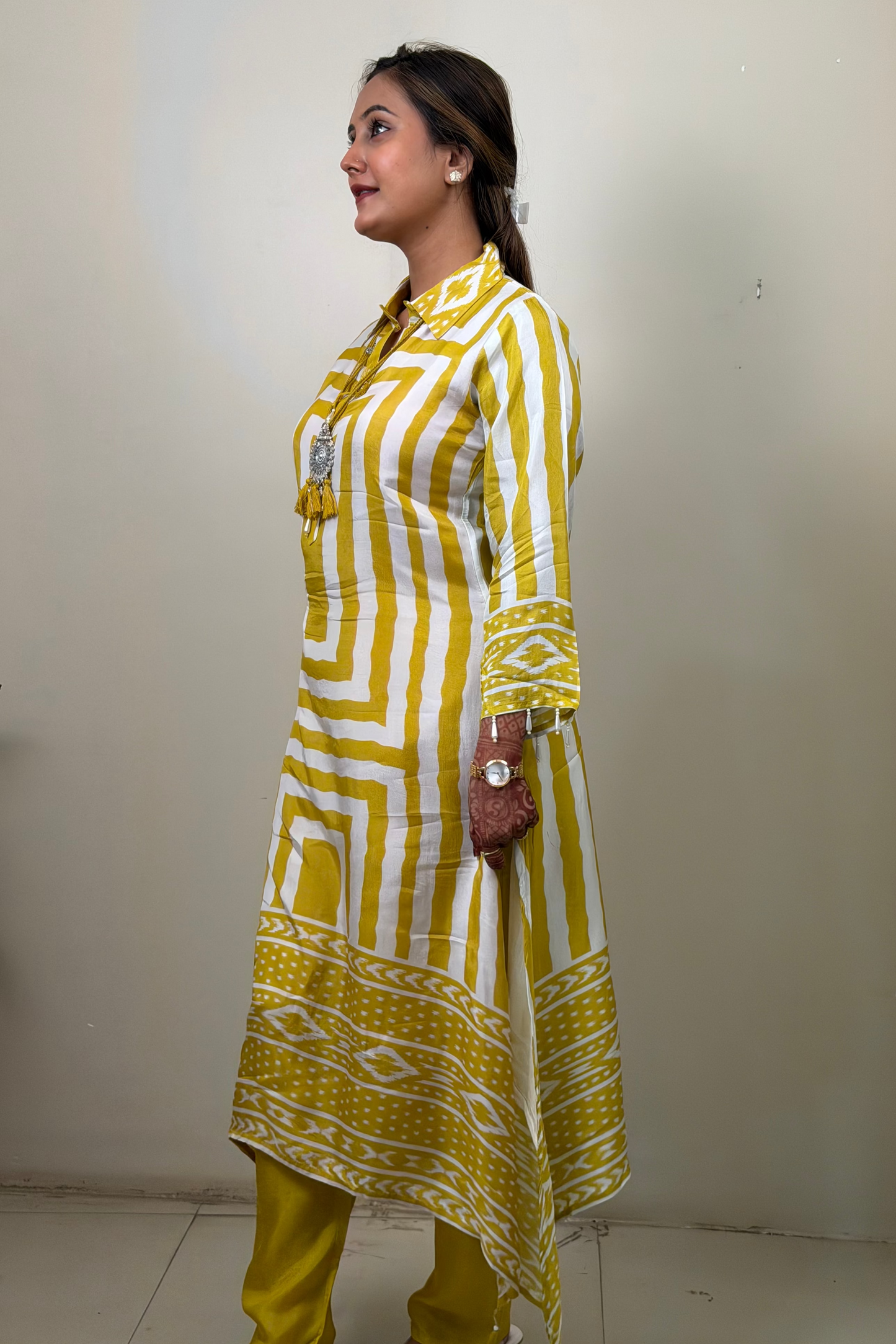 Woman wearing a yellow and white patterned kurta with pants against a plain background