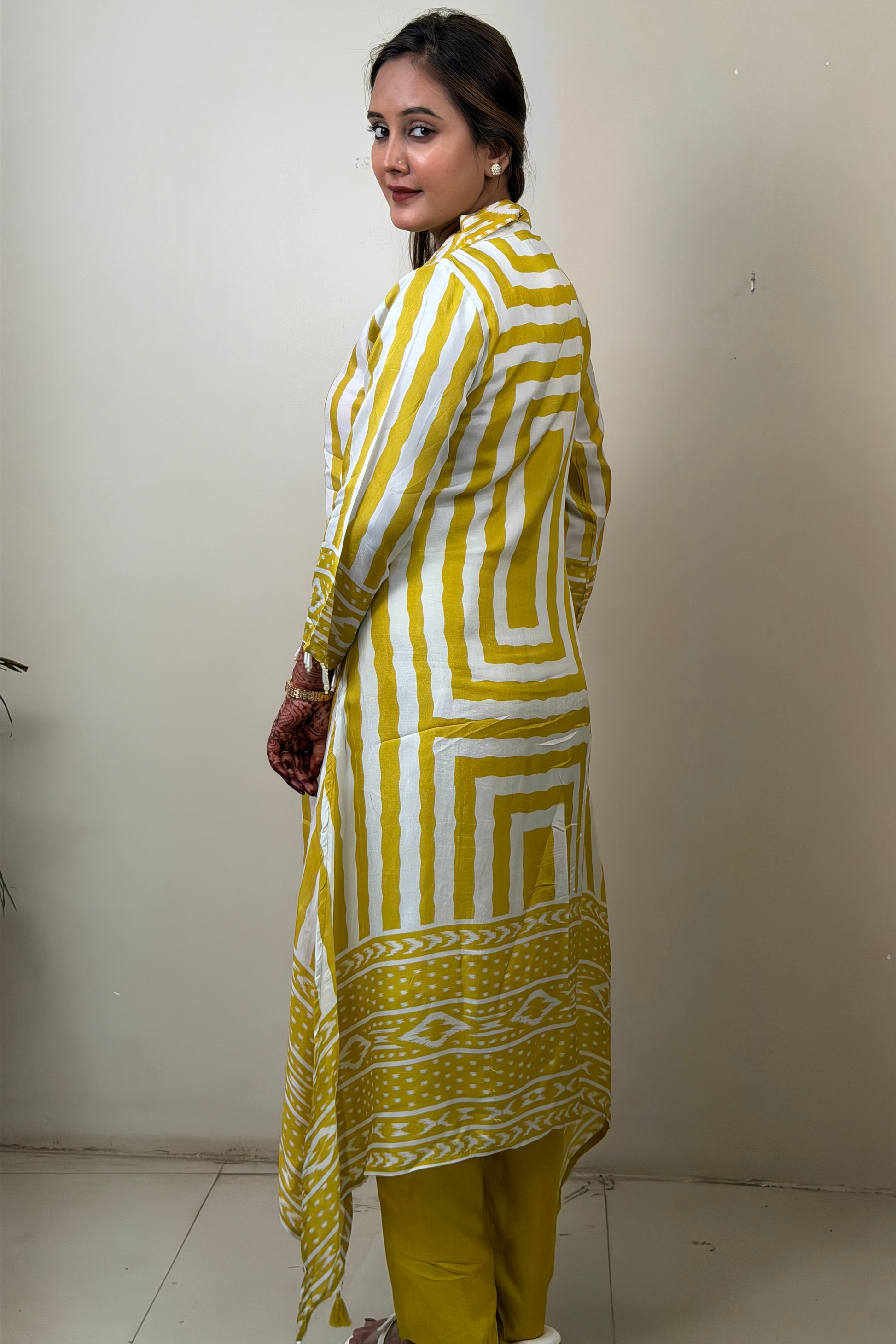 Woman wearing a yellow and white patterned kurta with yellow pants against a plain background