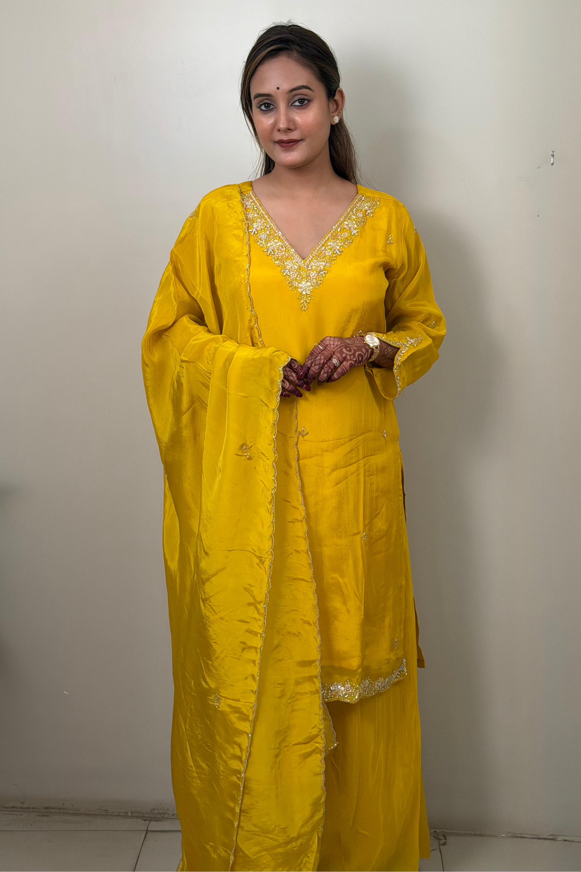 Woman wearing a yellow traditional outfit with intricate designs against a plain background