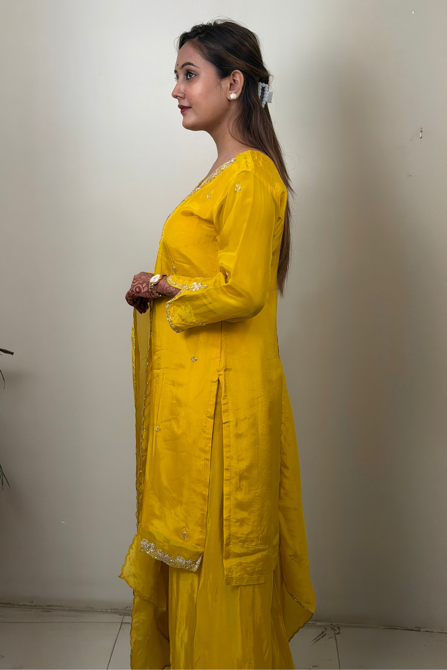Woman wearing a yellow traditional outfit standing against a plain wall.