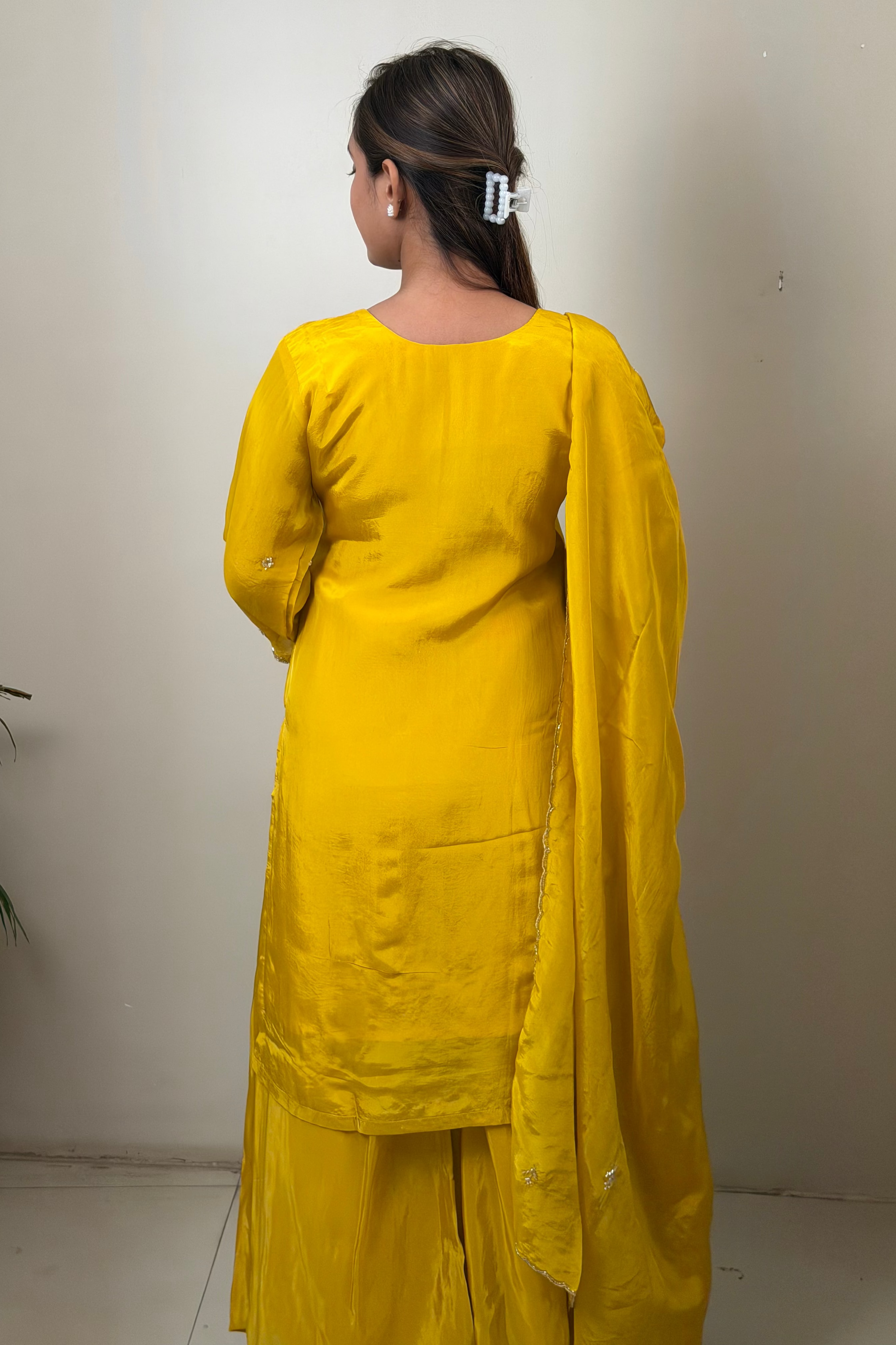 Person wearing a yellow traditional outfit standing against a plain wall.