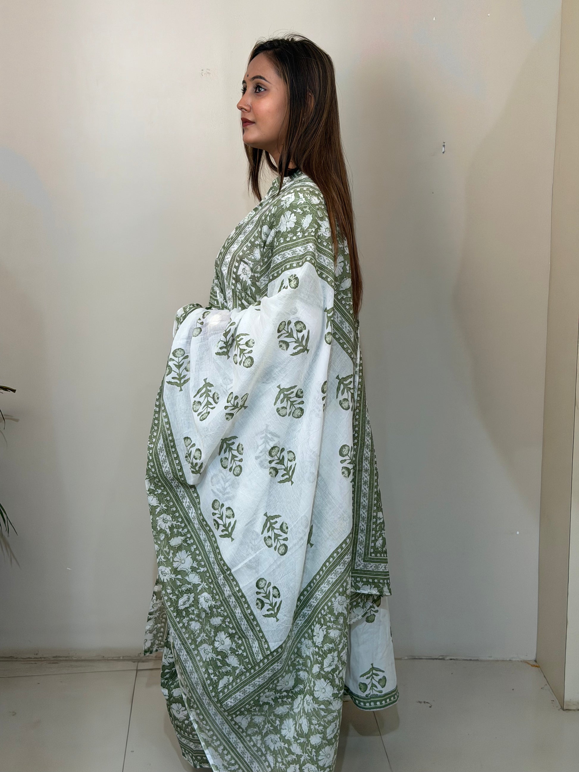 Woman wearing a white and green patterned shawl against a plain wall.