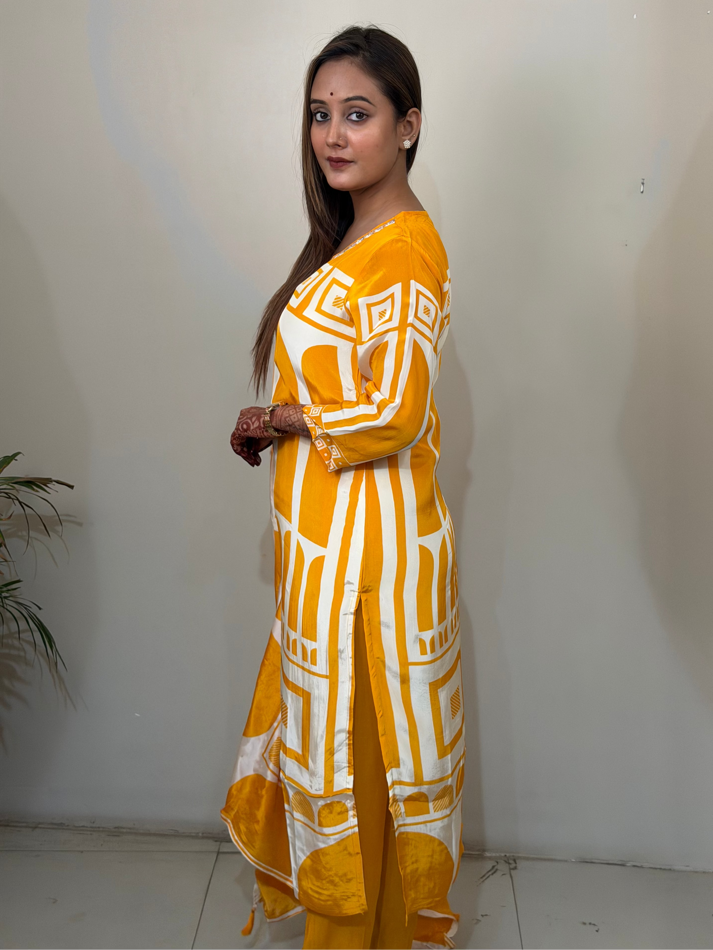 Woman wearing a yellow and white patterned outfit against a plain background