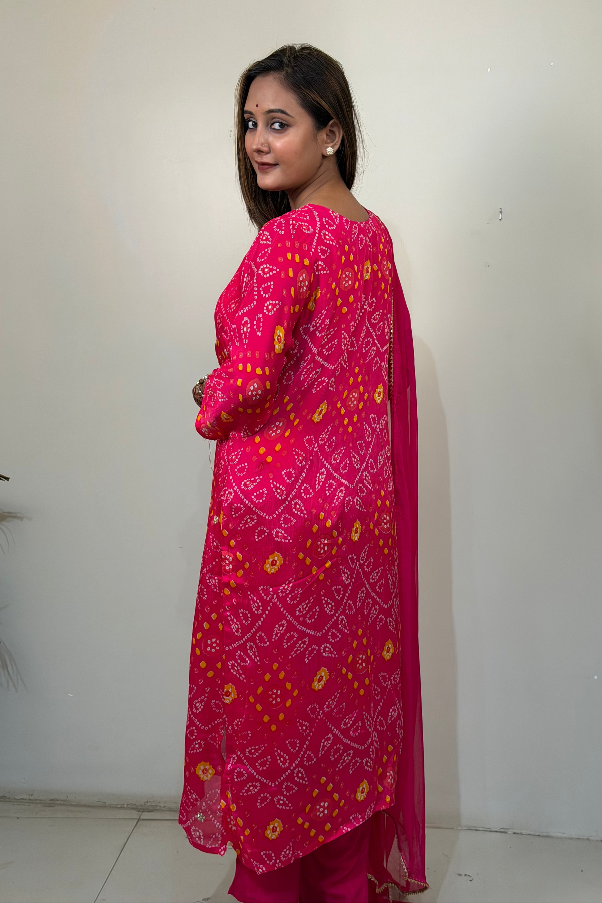 Woman wearing a bright pink traditional outfit with yellow patterns against a white wall.