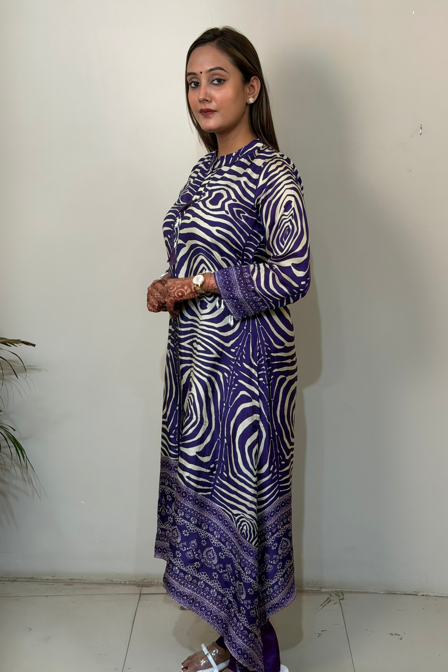 Woman wearing a long, patterned dress against a plain wall.