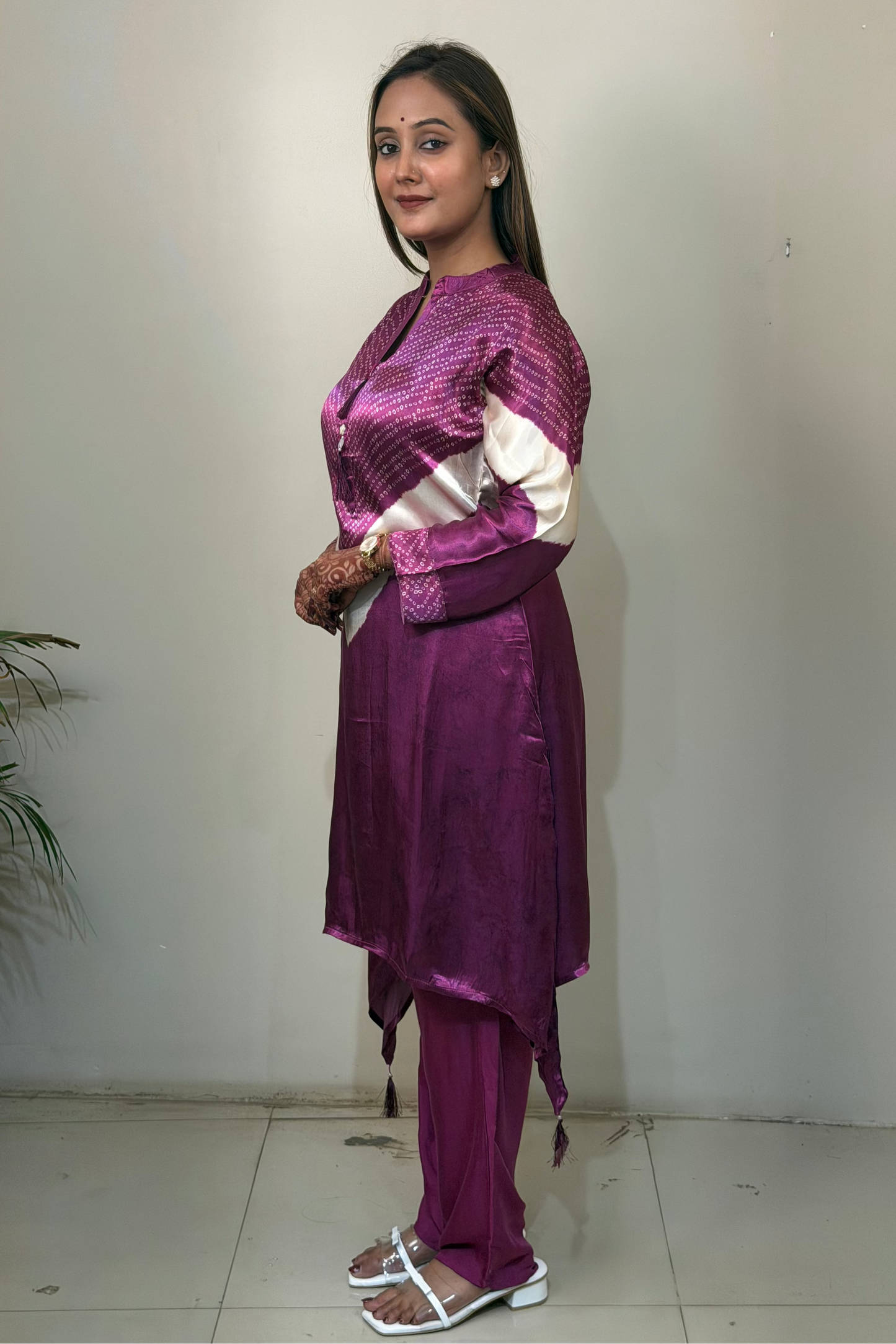 Woman wearing a purple traditional outfit standing against a white wall.