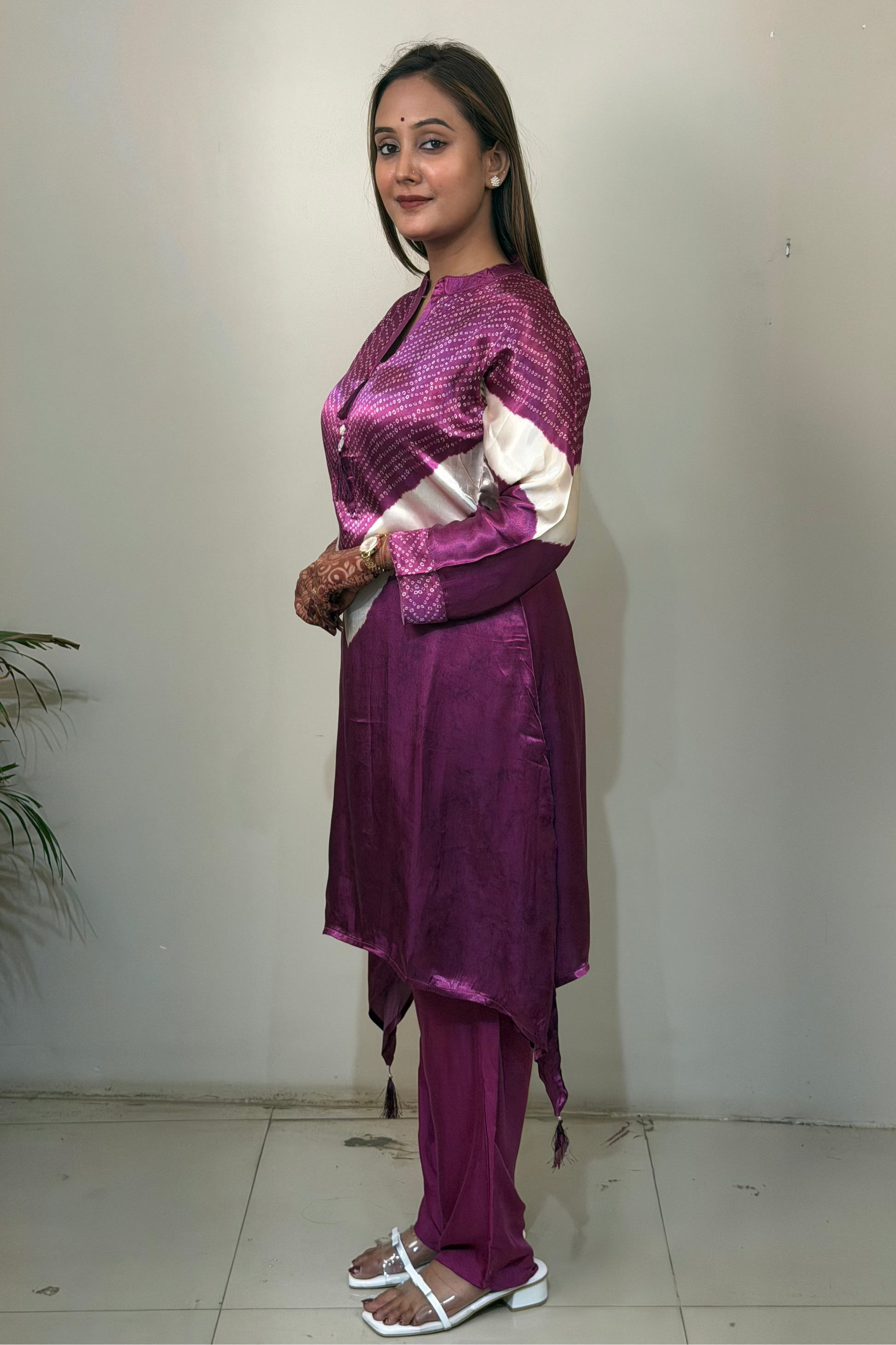 Woman wearing a purple traditional outfit standing against a white wall.